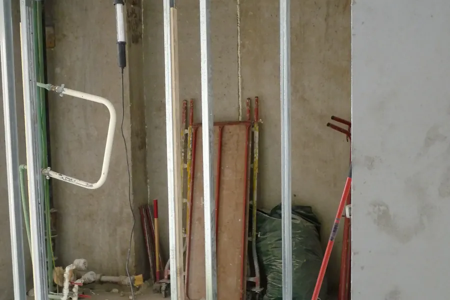 Ossature de cloison en rails métalliques montée devant un mur en béton, plaque de plâtre posée à droite